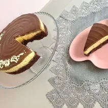 Foto da receita de torta bownie de maracujá, servida em um prato transparente, ao lado de um prato rosa em formato de coração, em uma mesa com uma toalha cinza