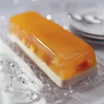 fotografia em tons de branco e laranja contém uma sobremesa gelada com camada de gelatina de frutas e pedaços de frutas.