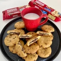 Fotografia de um prato preto servido de cookies e uma xícara vermelha com leite dentro.