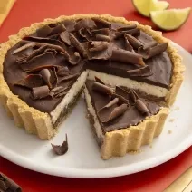 Foto da receita de Torta de Limão com Chocolate. Observa-se uma torta com cobertura de ganache e raspas de chocolate com um pedaço fatiado.
