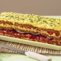 Foto da receita de Torta Fria Vegetariana. Observa-se a torta em um recipiente retangular com camadas de legumes e maionese. No topo, maionese com cheiro-verde bem picadinho.