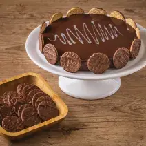 Imagem de uma torta decorada com biscoitos ao redor, disposta num prato branco alto, ao lado de uma tigela de madeira com mais biscoitos dentro
