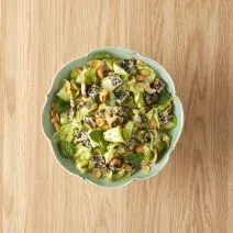 fotografia em tons de bege e verde de uma bancada vista de cima. Ao centro contém um recipiente redondo com salada de abobrinha.