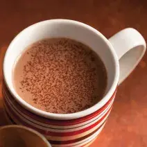 fotografia em tons de marrom e branco tirada de cima, contém uma xicara com chocolate quente.