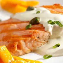 uma travessa branca contém um salmão com creme branco por cima e ao lado fatias de manga.