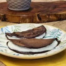 Fotografia em tons de marrom com um prato redondo ao centro. Em cima do prato existe duas panquecas de chocolate com aveia recheadas com um creme de iogurte.