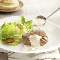 foto tirada de um prato redondo branco com um medalhão de filé com creme por cima e ao lado folhas de alface