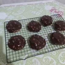 Foto da receita de Cookies low carb de chocolate. Observa-se uma grade preta com 7 cookies dispostos em cima, com calda de chocolate e chocolate em gotas na cobertura.
