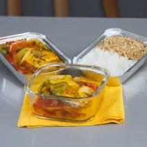 Foto da receita de Moqueca de Peixe Maggi, em um recipiente de vidro e alumínio, sobre um pano amarelo, em uma bancada
