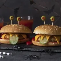 Fotografia de um hamburguer com carinha de "monstro", mostrando as camadas de frango empanado, pepino, queijo.