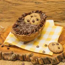 Fotografia em tons de marrom de uma bancada marrom com uma tábua de madeira com um paninho amarelo e branco, sobre ele um ovo recheado de cookie. Ao lado um cookie.