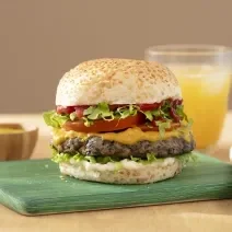 Foto da receita de Hambúrguer de Cogumelo. Observa-se um lanche montado com pão de hambúrguer com gergelim, mostarda, ketchup, alface, tomate e o hambúrguer de cogumelo ao meio.
