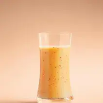 Fotografia em tons de laranja em um fundo laranja e um copo de vidro alto e largo com o suco de acerola, maracujá, pêssego e laranja dentro dele.