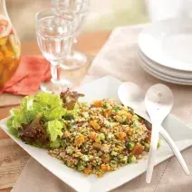 uma mesa contém duas taças de vidro, pratos e um prato quadrado com a salada de sevadinha e duas colheres ao lado.