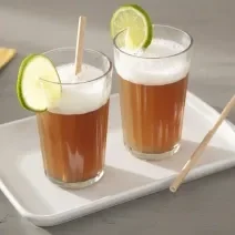 Foto da receita de Suco de Mate com Limão. Observa-se dois copos decorados com uma rodela de limão e com a bebida dentro