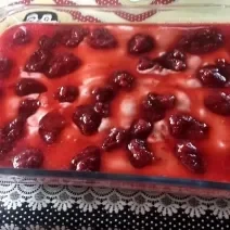 Foto em tons de vermelho da receita de mousse de frutas servida em um refratário de vidro grande com calda de frutas vermelhas por cima