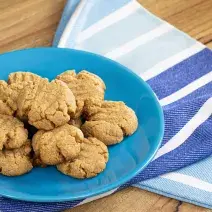 fotografia em tons de marrom e azul de uma bancada marrom vista de cima, contém um pano em tons de azul com branco e por cima um prato redondo azul com biscoitinhos.