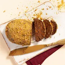 Foto vista de cima da receita de Ovo Fudge Crocante, cortado em algumas fatias, sobre uma tábua branca e com uma faca dourada ao lado.