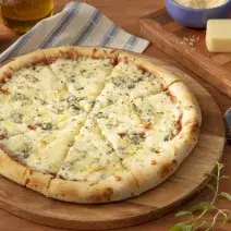 Fotografia em tons de azul em uma bancada de madeira, um pano azul listrado, uma tábua de madeira de pizza, um cortador de pizza ao lado e pedaços de queijo.