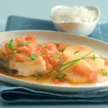 Fotografia em tons de azul e laranja, ao centro um pano azul e acima dele um prato branco com pedaços de peixe e ao lado um potinho com arroz.
