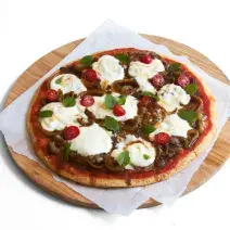 Ao centro, uma tábua de madeira marrom redonda com um pano branco e uma pizza com tomates, cebolas e iogurte por cima.