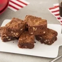 Foto da receita de Brownie de Café. Observa-se 5 pedaços de brownie dispostos um em cima do outro sobre um prato branco. Ao lado direito, uma xícara de café para acompanhar.