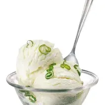 Fotografia em tons de branco em um fundo branco com um pote de sorvete de vidro com o sorvete de leite Moça dentro, com raspas de limão e uma colher.