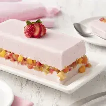 fundo de madeira branca com paninho rosa claro, um prato branco com uma camada de gelatina com iogurte de morango, uma camada de salada de frutas e mais uma camada de gelatina com iogurte de morango.