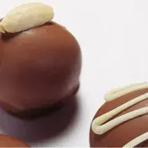 fotografia em tons de branco e marrom de uma bancada branca vista de cima que contém 3 bombons de chocolate