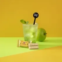 Foto da receita de Soda Italiana Apple Green. Observa-se um fundo amarelado e verde com um copo alto no centro, decorado com folha de hortelã. Uma maçã verde atrás do copo decora a foto.