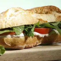 Em uma bancada contém um sanduíche recheado com patê de Requeijão Cremoso NESTLÉ e atum com rúcula e tomate