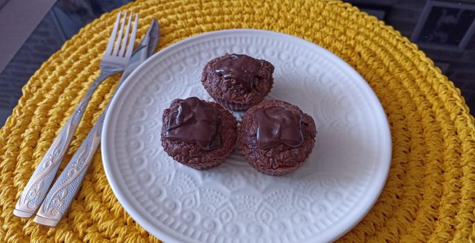 Imagem da receita de Muffin de cacau com coco e cobertura de chocolate meio amargo, em um prato branco, sobre uma mesa e ao lado os talheres