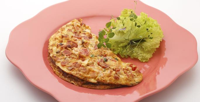 Foto de um prato rosa com um omelete em cima e algumas folhas de alface decorando