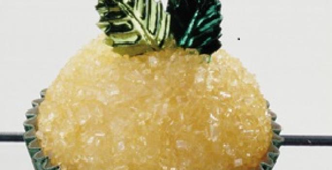 Fotografia em tons de amarelo e verve de um docinho em uma forminha verde, decorado com açúcar e duas folhinhas verdes.
