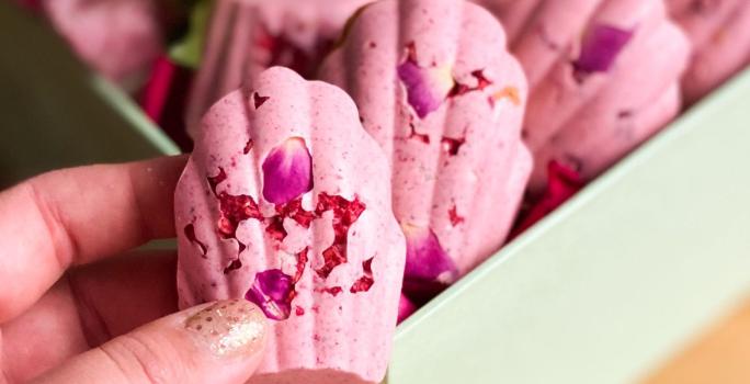 Fotografia em tons de rosa com vários doces cor de rosa ao centro. Esses doces possuem formato de concha e estão dispostos lado a lado.
