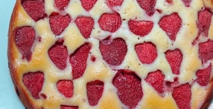 Foto da receita de Bolo de Iogurte e Morango. Observa-se um bolo redondo assado com morangos cortados ao meio no topo.
