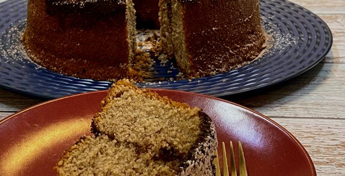 Foto da receita de Bolo com Farofa de Canela. Observa-se um prato de sobremesa com uma fatia do bolo e um garfinho e, atrás, o bolo maior em um prato grande azul.