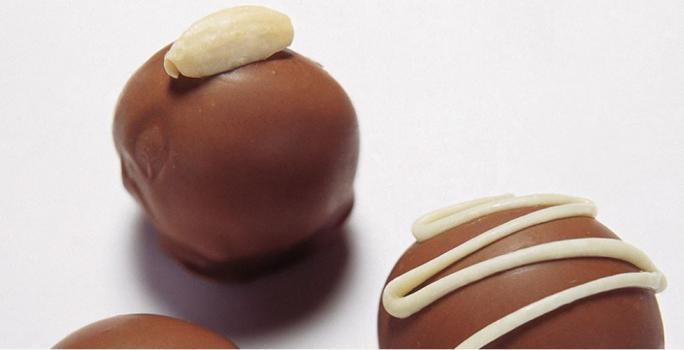 fotografia em tons de branco e marrom de uma bancada branca vista de cima que contém 3 bombons de chocolate