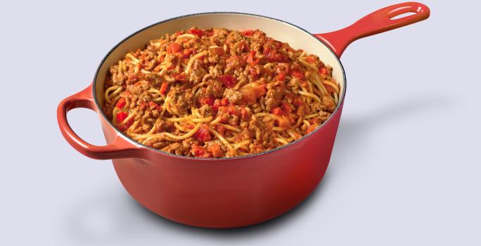 Fotografia em tons de vermelho e marrom de uma panela vermelha com macarrão espaguete ao molho bolonhesa dentro.