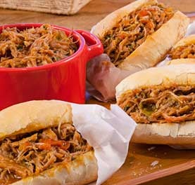 Panela com carne desfiada ao molho ao lado de três pães franceses recheados com a mesma carne. Panela com carne desfiada ao molho ao lado de três pães franceses recheados com a mesma carne.