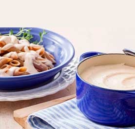 Panela com molho branco ao lado de um prato de macarrão coberto com o mesmo molho. Panela com molho branco ao lado de um prato de macarrão coberto com o mesmo molho.