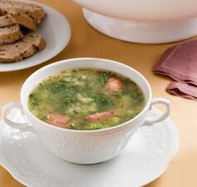 Tigela branca contendo sopa com couve picada e pedaços de linguiça ao lado de prato com pão. Tigela branca contendo sopa com couve picada e pedaços de linguiça ao lado de prato com pão.