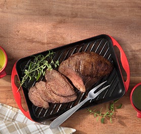 Peça de carne fatiada sobre uma grelha ao lado de um garfo trinchante sobre mesa de madeira. Peça de carne fatiada sobre uma grelha ao lado de um garfo trinchante sobre mesa de madeira.