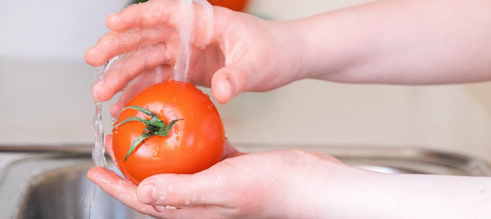 Como higienizar frutas, verduras e alimentos: uma pessoa lavando um tomate na pia
