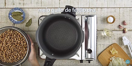 Foto tirada de cima mostra uma panela vazia ao lado de uma vasilha com feijão e uma tábua com alho picado