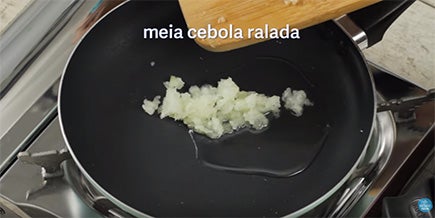 Em uma frigideira, há um punhado de cebola ralada e óleo