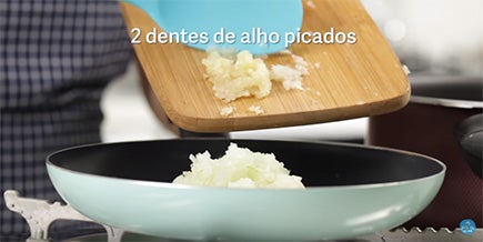Pessoa joga alho picado de uma taboa na frigideira