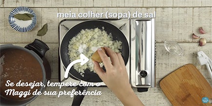 Pessoa joga sal sobre a frigideira com alho e cebola picados