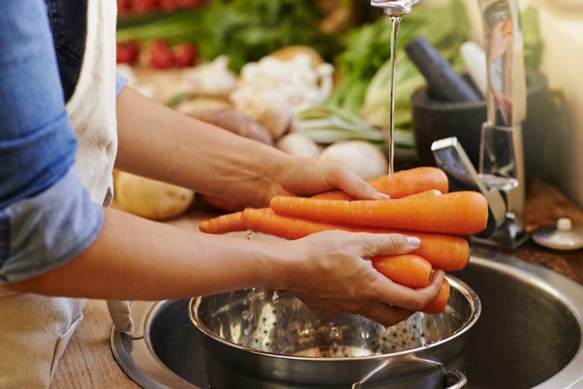 Benefícios da Cenoura: Uma pessoa lavando cenouras na pia