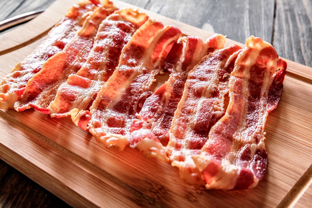 Bacon: O que é, Como Fazer e Melhores Receitas! Bacon: Fatias de bacon na tábua de madeira